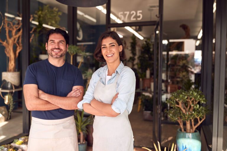 Professional men and women in aprons smile in front of a gardening store