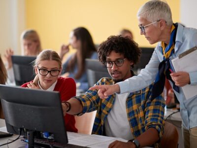Female professor checking students work at an informatics lecture in the university computer classroom