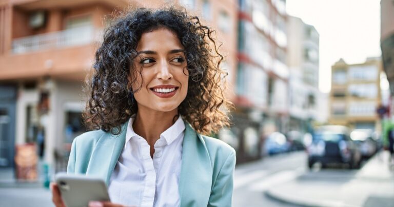Young hispanic business woman wearing professional look smiling confident at the city using smartphone